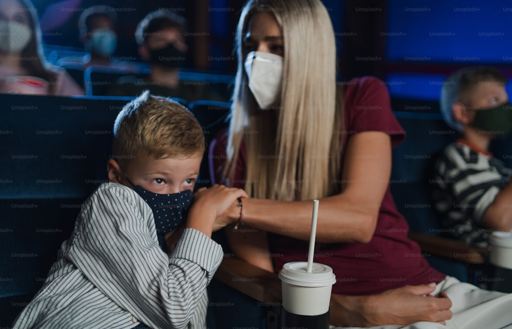 A worried small boy with mother in the cinema while watching film, coronavirus concept.