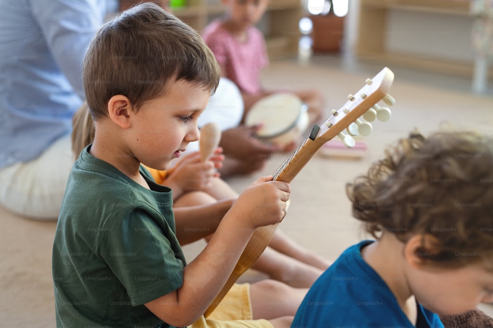Eine Gruppe kleiner Kindergartenkinder sitzt drinnen im Klassenzimmer auf dem Boden und spielt Musikinstrumente.