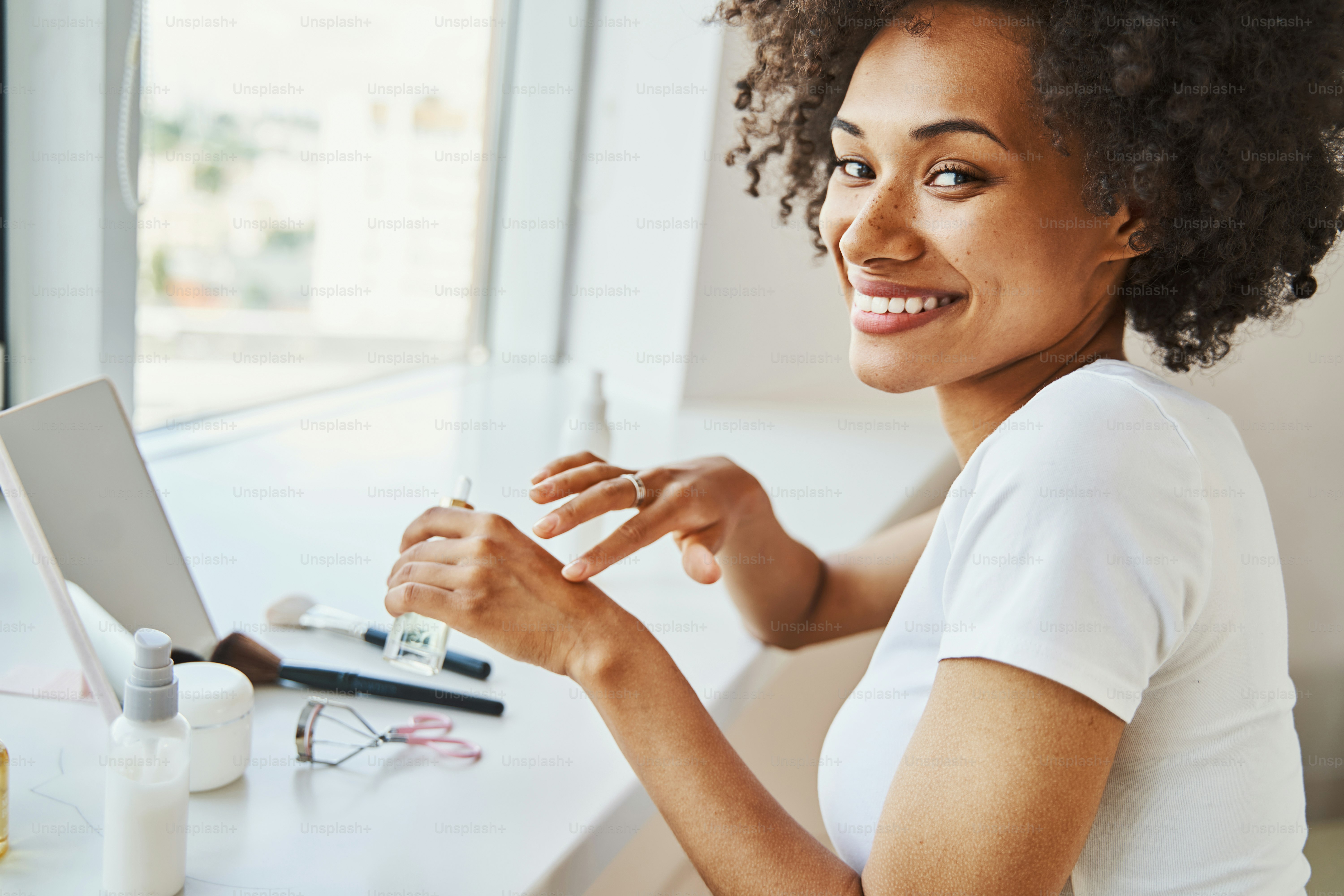 Portrait of a smiling happy beautiful curly-haired lady massaging a moisturizing hand lotion into her dry skin