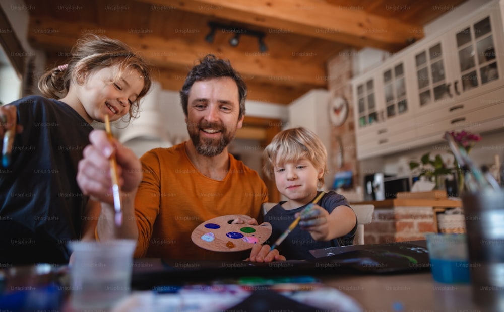 Ein reifer Vater mit zwei kleinen Kindern, die sich zu Hause ausruhen und Bilder malen.
