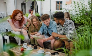Un grupo de jóvenes felices sentados en un café al aire libre en un viaje a la ciudad, usando el mapa.