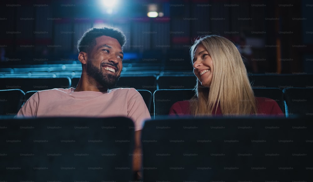 Una vista frontal de una pareja joven y alegre en el cine, viendo películas y hablando.