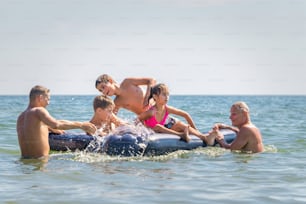 Cheerful and happy family on vacation at the seaside. Father and grandfather playing with children in the sea waves. Summer travel and outdoor vacations, healthy lifestyle