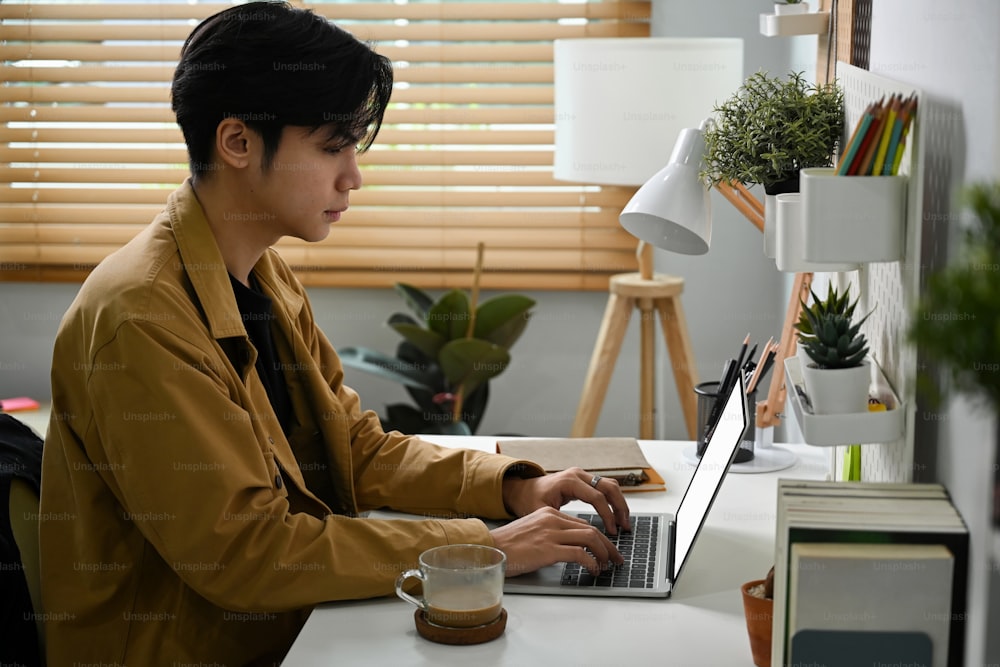 Young Asian man sitting in home office and working with computer laptop.