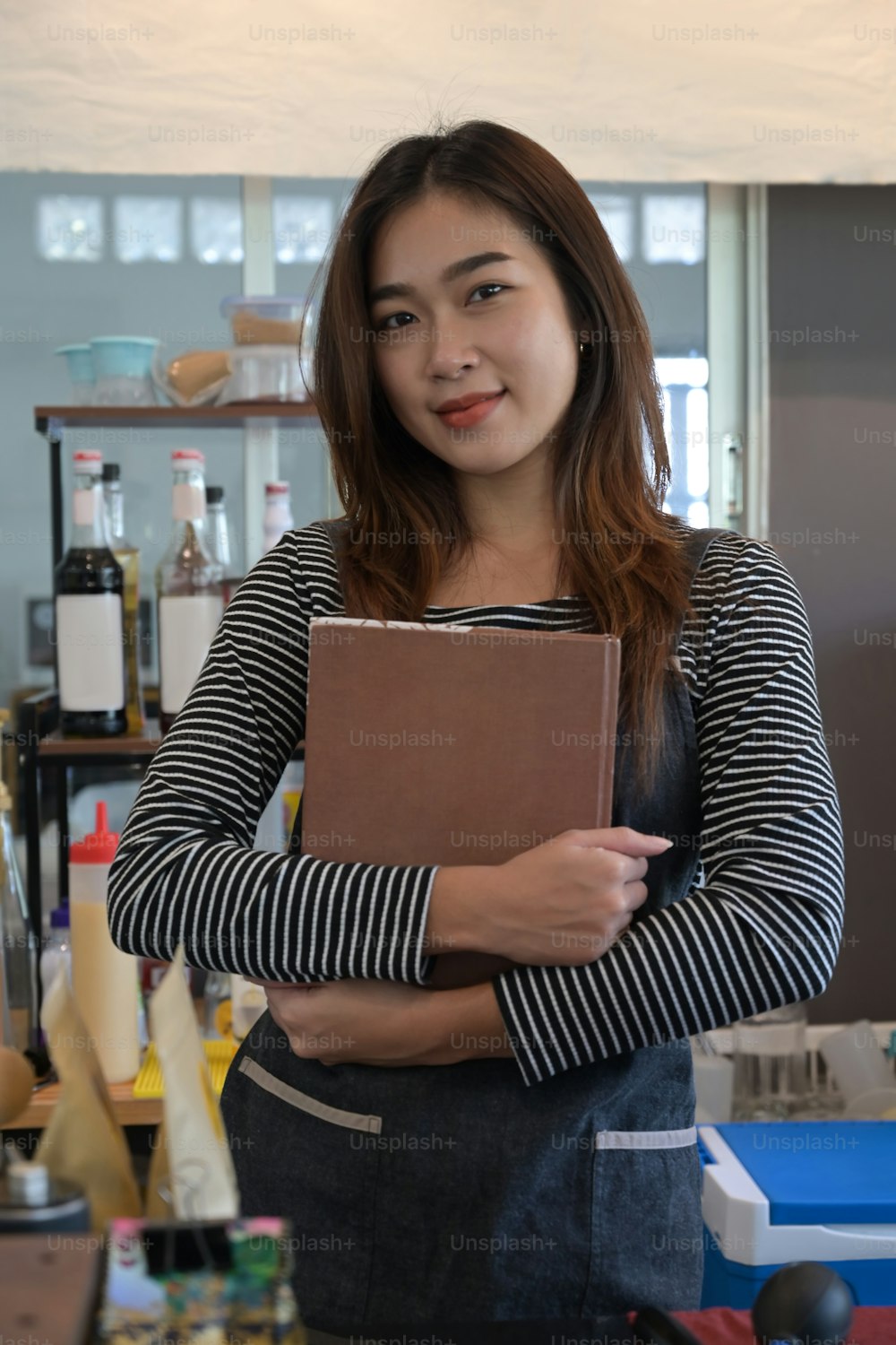 Portrait of female barista holding menu and smiling to camera.