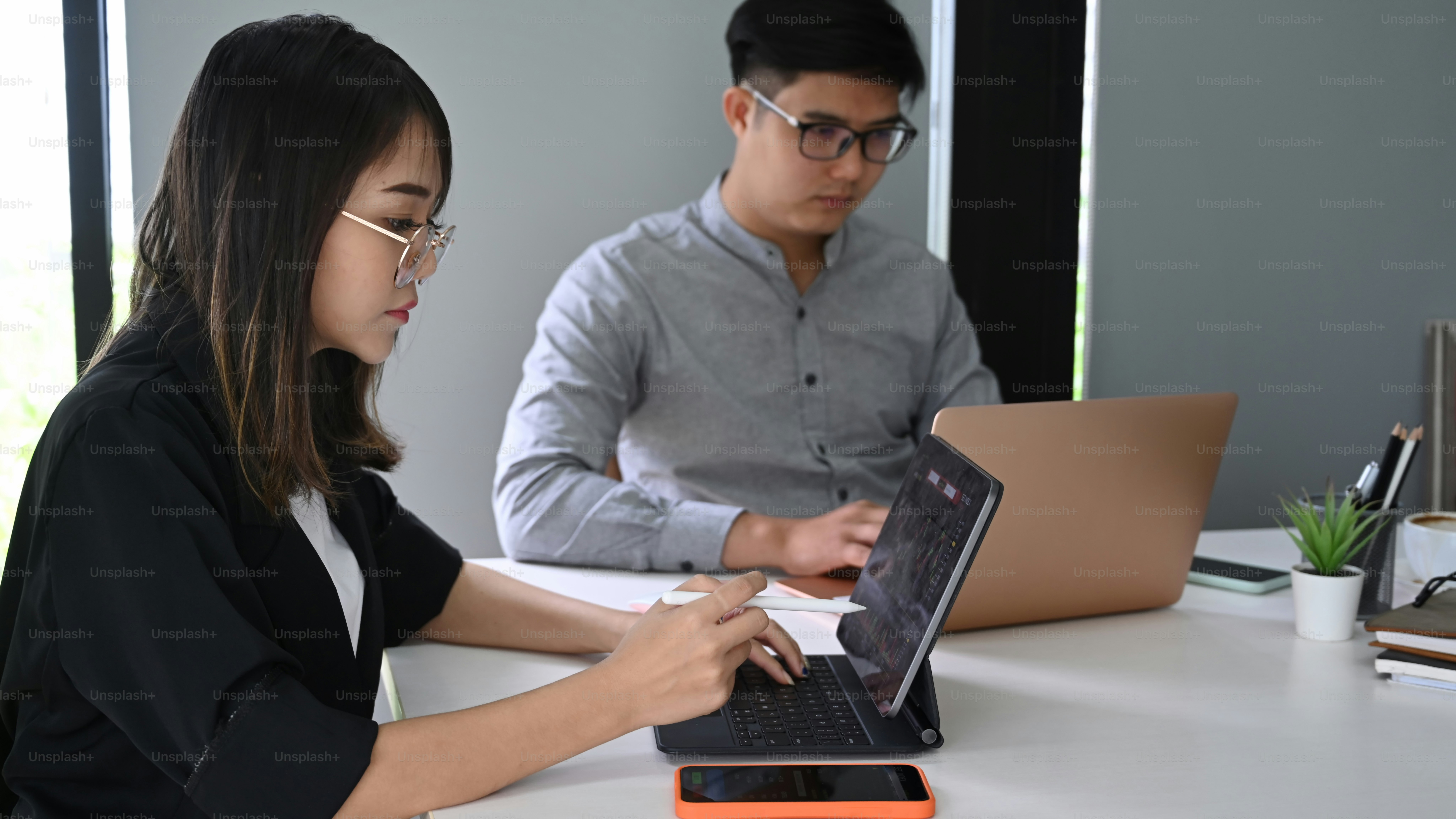 Businesspeople analyzing stock charts on computer tablet while sitting in modern workplace.