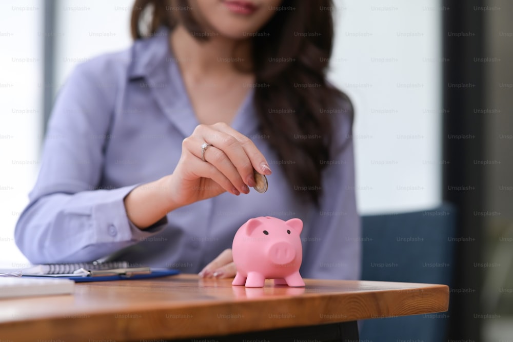 Asiatische Frau, die Münze ins Sparschwein steckt. Geld sparen und finanzielles Konzept.