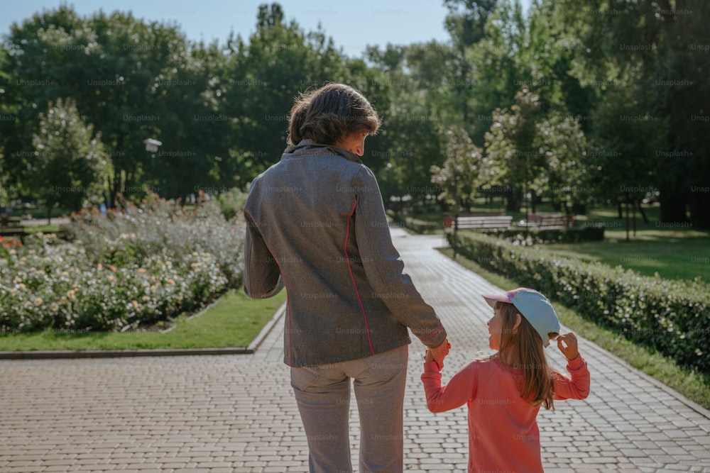 Happy grandmother and granddaughter walking in the park, view from the back.