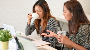 Asian young businesswomen working with laptop computer and drinking coffee at cafe co-working space, business talk, working together