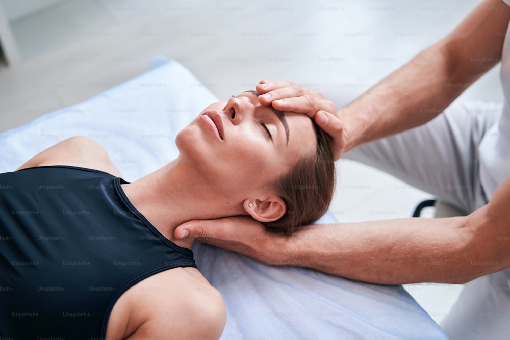 Close up side view portrait of charming young Caucasian female patient lying on massage table while receiving spa treatment in rehabilitation center