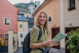 A happy young woman tourist outdoors on trip in town, using map.