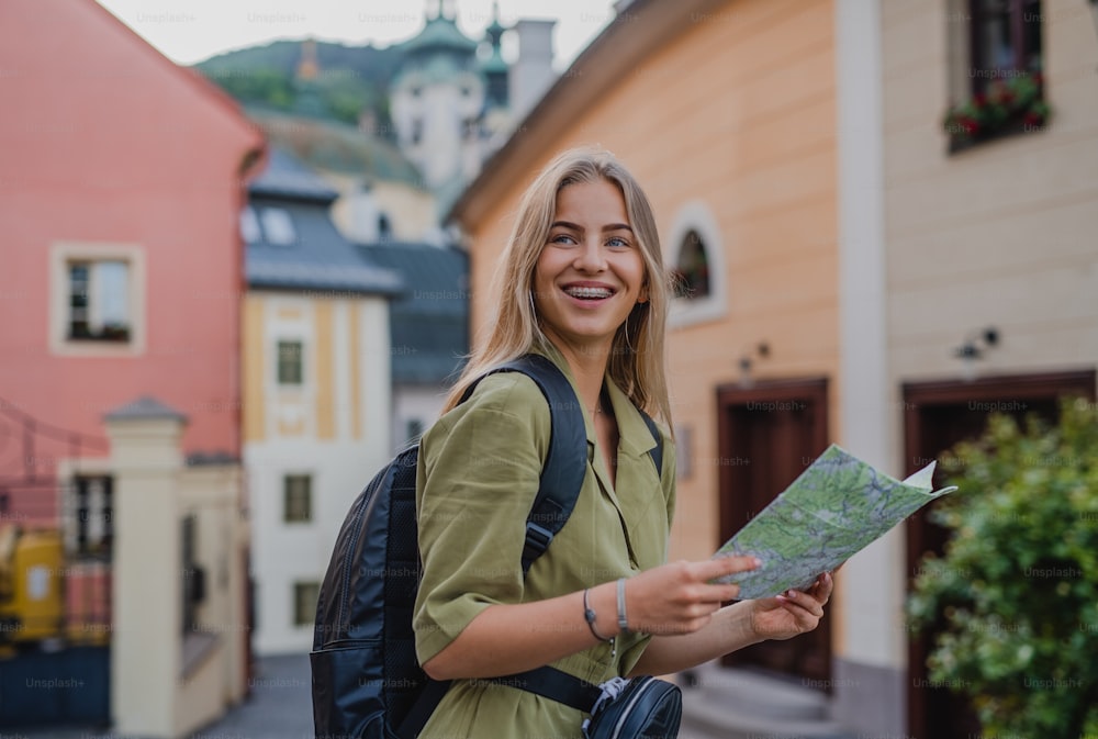 A happy young woman tourist outdoors on trip in town, using map.