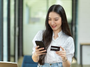 Online payment concept, young woman using smartphone to pay via online payment application, online banking service, phone and credit card in hands