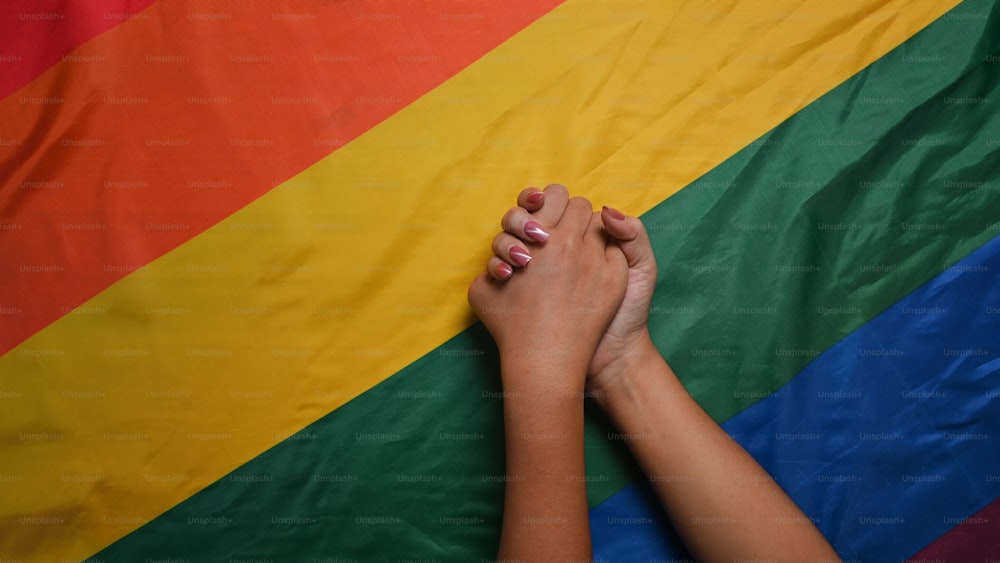 젊은 아시아 여성 LGBT 레즈비언 커플이 LGBT 프라이드 깃발 위에 손을 들고 있다.