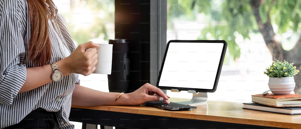 一杯のコーヒーを持ち、デジタル タブレットを使用している女性の手。コーヒー ショップ フリーランス コンセプトで働く女性。の写真 – テーブル  Unsplashの写真