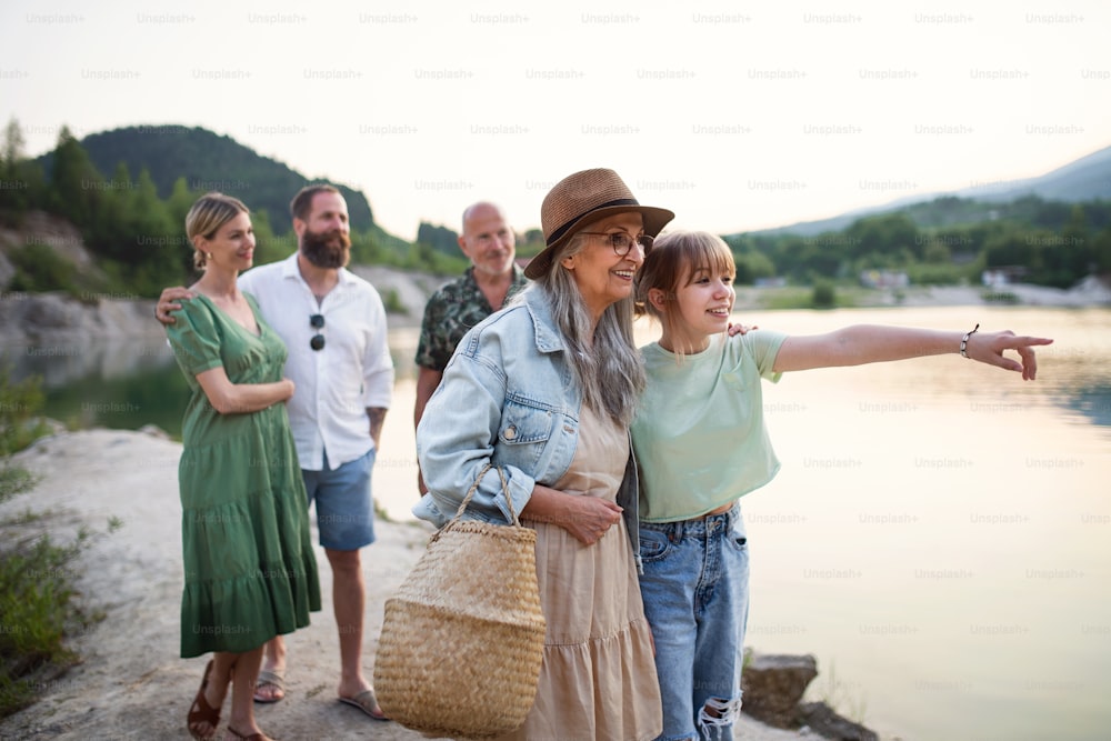 Ritratto di felice famiglia multigenerazionale in vacanza estiva, camminando in riva al lago.