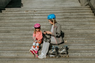 Active happy grandmother and granddaughter are preparing for roller skating sitting on the steps of the stairs in the street.