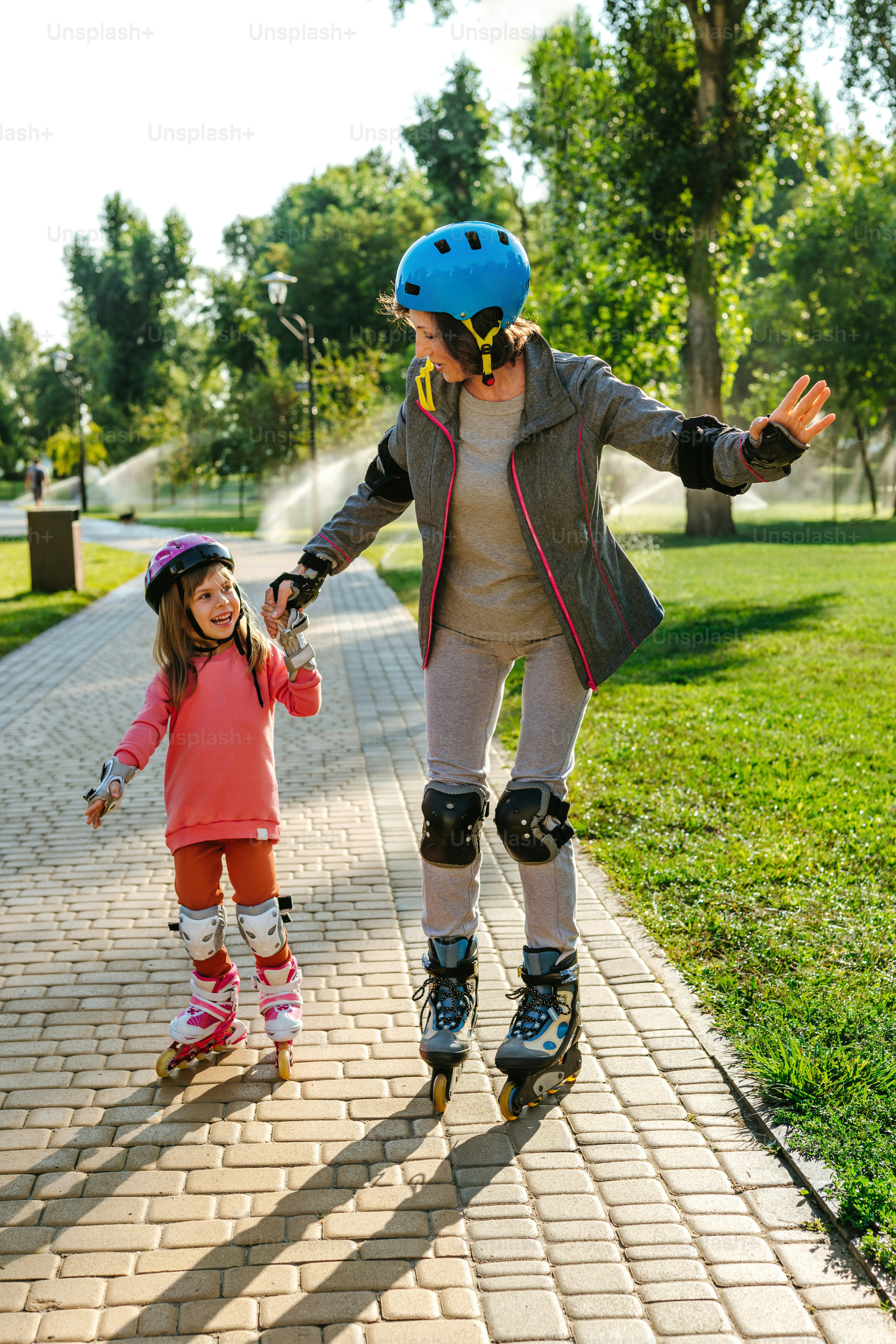 Active happy grandmother and granddaughter having fun time together during roller skating in the park.