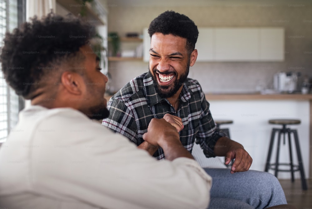 A portrait of young adult brothers on sofa indoors at home, giving fist bump.