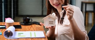 Female estate agent holding house keys and house model. Real estate and mortgage investment.
