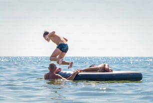 Cheerful and happy family on vacation at the seaside. Father and grandfather playing with children in the sea waves. Summer travel and outdoor vacations, healthy lifestyle