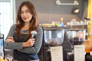 カウンターの前に立ち、コーヒーショップ、カフェでポルタフィルター、コーヒーフィルターを保持する魅力的な美しさのアジアの女性バリスタ