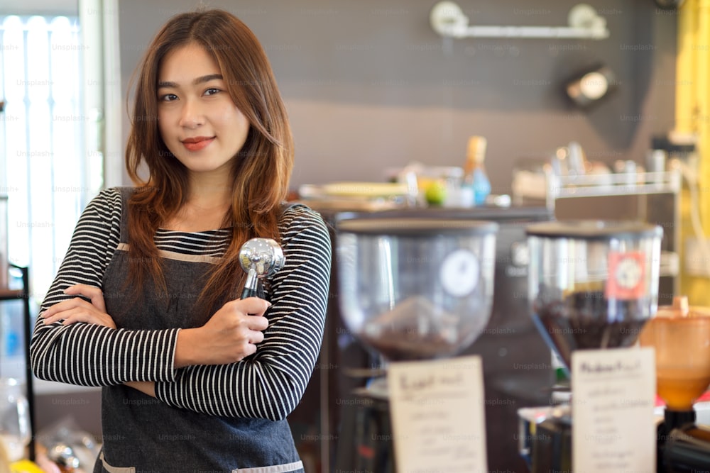 Barista asiática de belleza atractiva de pie frente al mostrador y sosteniendo portafiltro, filtro de café en cafetería, cafetería