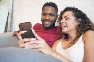 Young couple using a mobile phone together while sitting on a couch at home.