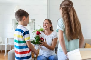 Happy children giving gift an flowers to mother. Happy Mothers Day! Children boy and girl congratulate smiling mother, give her flowers bouquet of roses and a gift box during holiday celebration