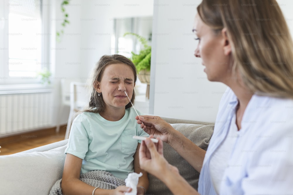 La madre está llevando la prueba rápida de covid-19 en casa a su hija enferma en casa. Madre realizando hisopado nasal a su hijo tomando ejemplo para analizar si el paciente es positivo para las enfermedades infecciosas