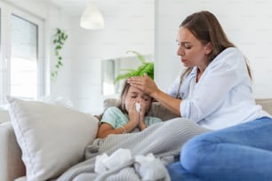 病気の子供の体温を測る母親。高熱を出した病気の子供がベッドに横たわり、母親が体温計を持っている。額に手を当てる。