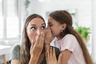 Close up image amazed mother hears incredible news from little daughter, kid girl share secret telling something interesting while mom open mouth feels surprised, trust, confidant person, fun concept