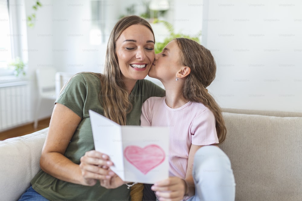Happy mother's day! Child daughter congratulates mom and gives her postcard. Mum and girl smiling and hugging. Family holiday and togetherness.