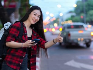 Attraente giovane viaggiatrice femminile che fa segno a mano per chiamare taxi sulla strada della città, viaggiatore solitario, luce notturna sulla strada
