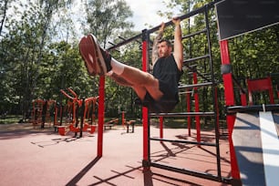 Ángulo bajo de hombre guapo atlético usando barra horizontal para hacer abdominales abdominales durante el entrenamiento al aire libre