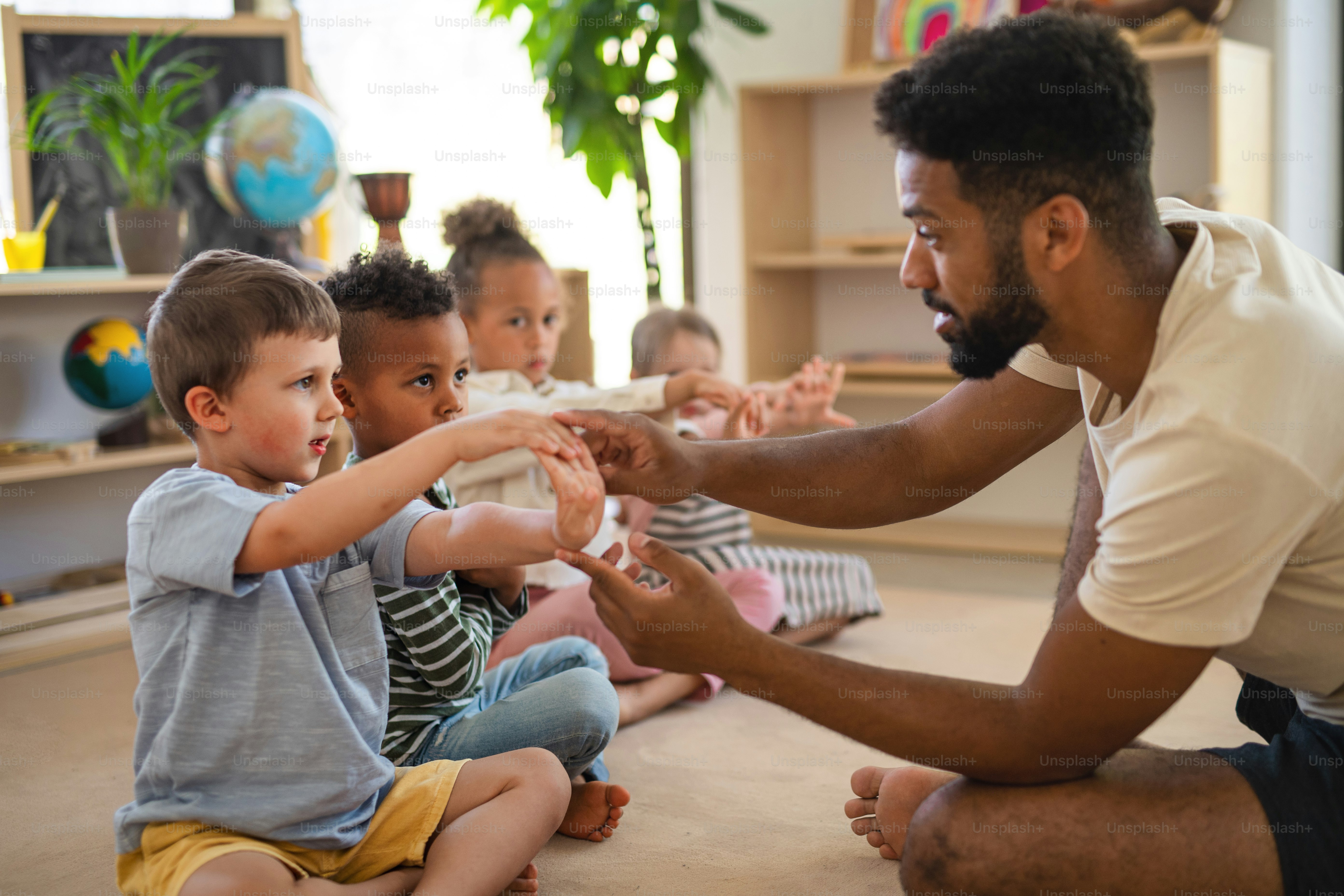 Un groupe de petits enfants de maternelle avec un enseignant assis par terre à l’intérieur de la salle de classe, faisant de l’exercice