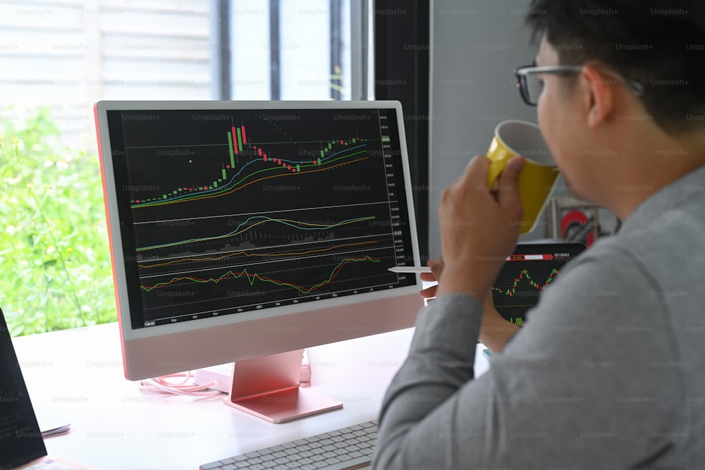 Businessman drinking coffee and checking stock market on desktop computer.