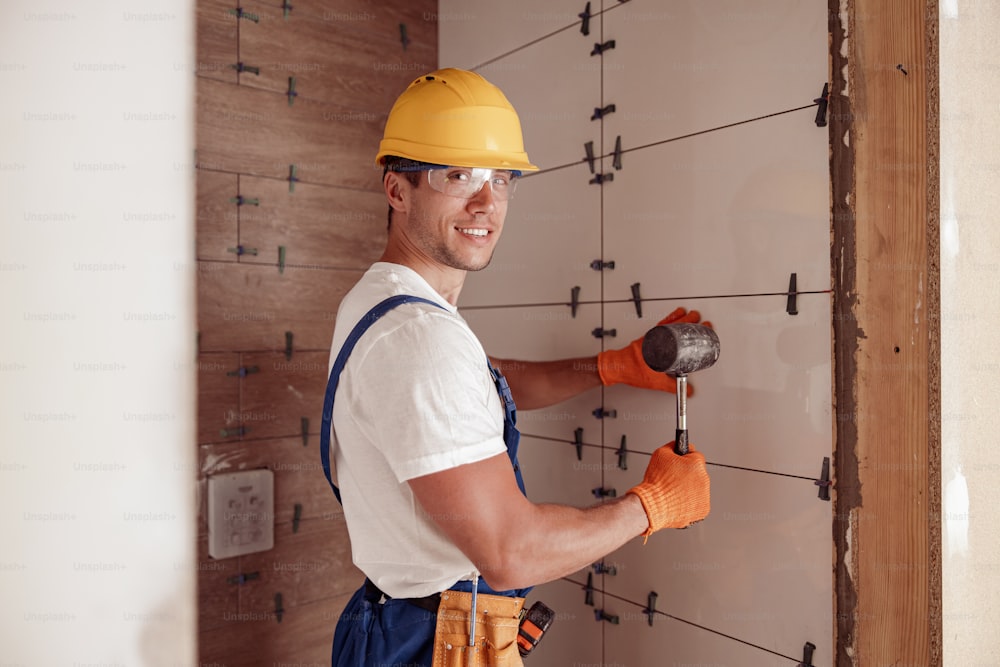 Cheerful young man construction worker looking at camera and smiling while holding rubber hammer