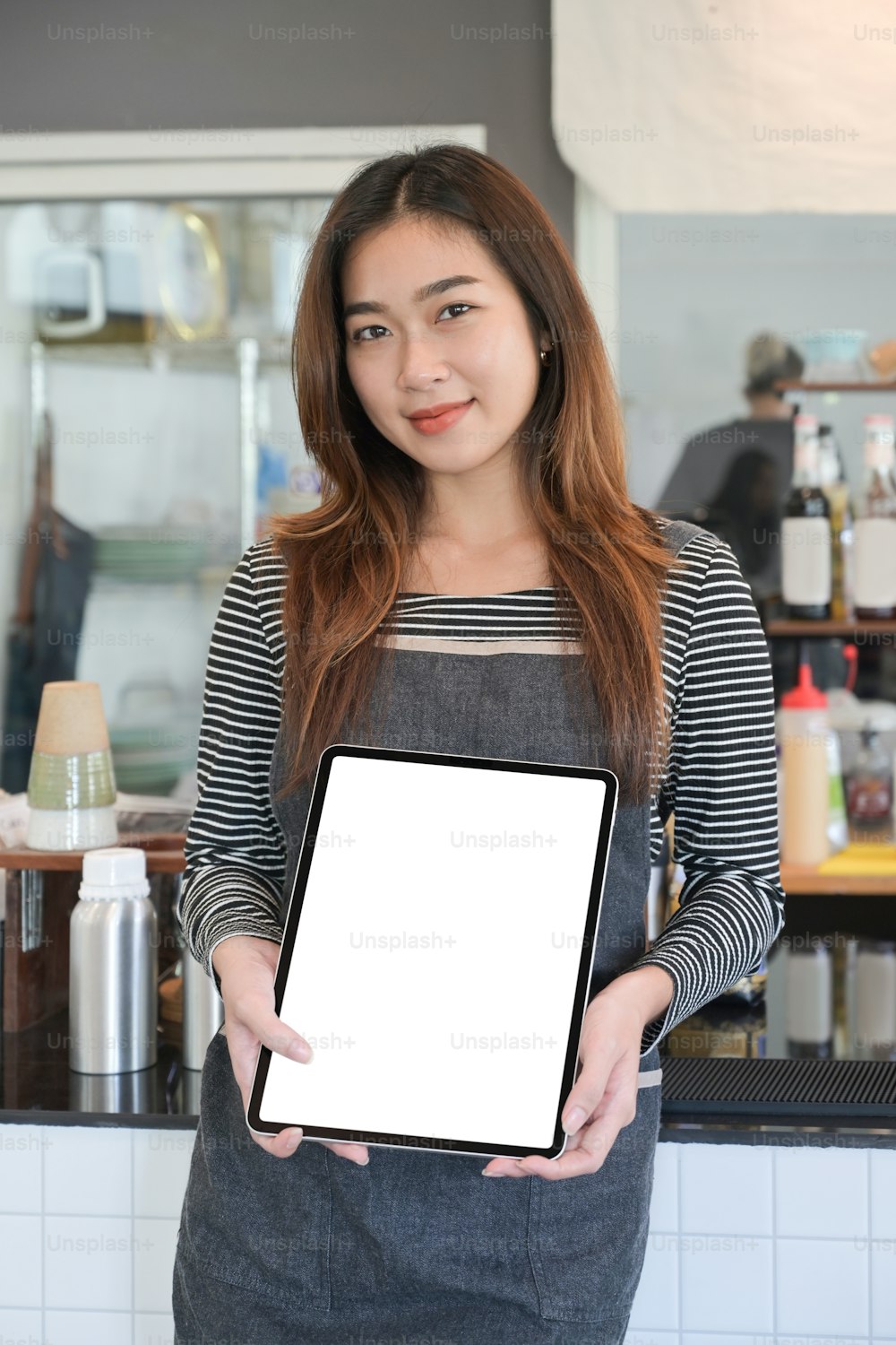 Portrait of smiling female entrepreneur showing digital tablet while standing at the counter in her coffee shop.