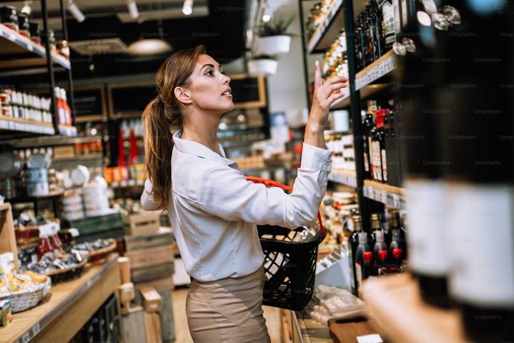 Schöne junge und elegante Frau, die im modernen Supermarkt oder Lebensmittelgeschäft gesundes Essen und Trinken kauft. Lifestyle- und Konsumkonzept.