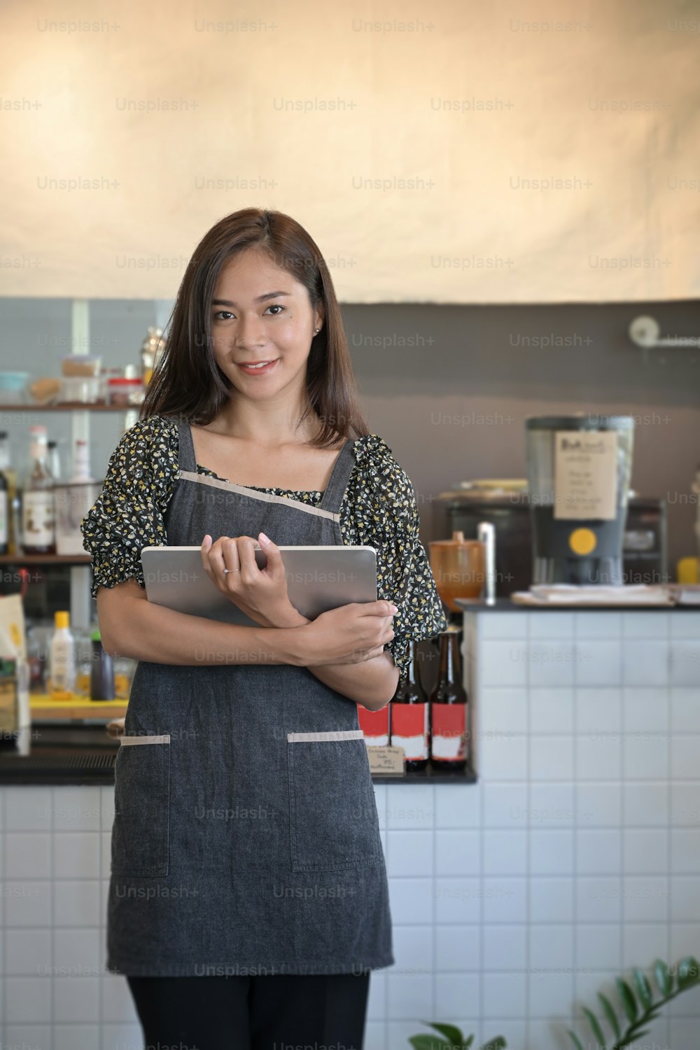 Portrait of smiling female entrepreneur in apron holding digital tablet and standing in her trendy cafe.