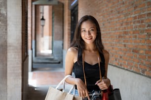 Young Asian woman traveler holding her shopping bags and smiling to camera.