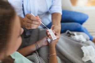 Mother is taking rapid covid-19 test at home to her sick daughter at home. Mother performing nasal swab on her child taking example to analyze if patient is positive for the infectious diseas
