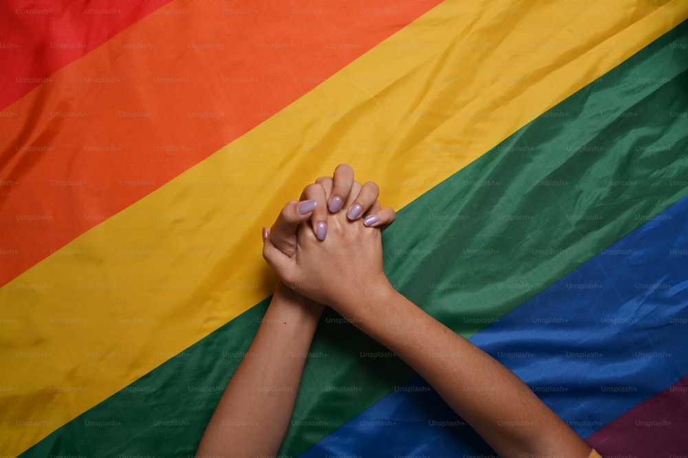 LGBT 프라이드 깃발 위에 손을 들고 있는 두 여성 레즈비언 커플. LGBT 개념.