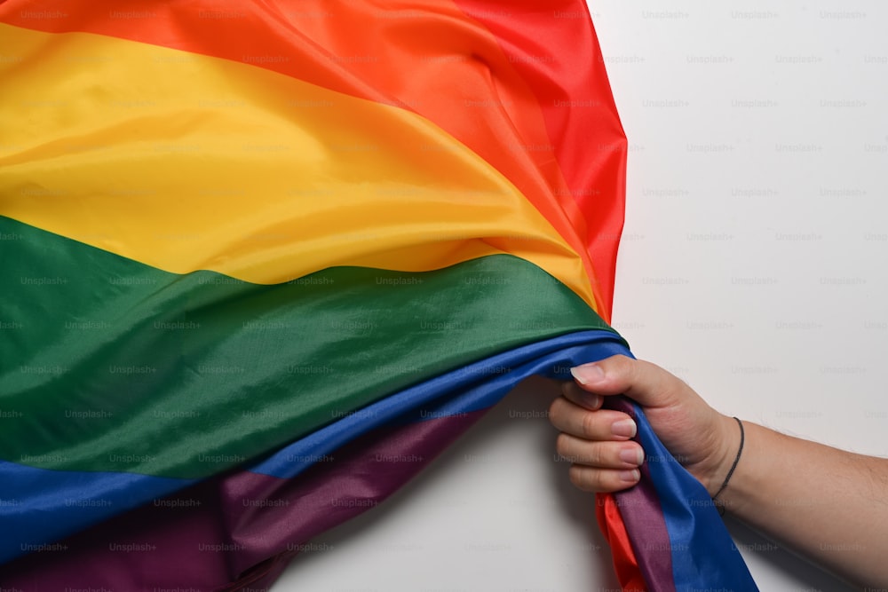 Mano del hombre sosteniendo la bandera del orgullo LGBT sobre fondo blanco. Concepto LGBT.