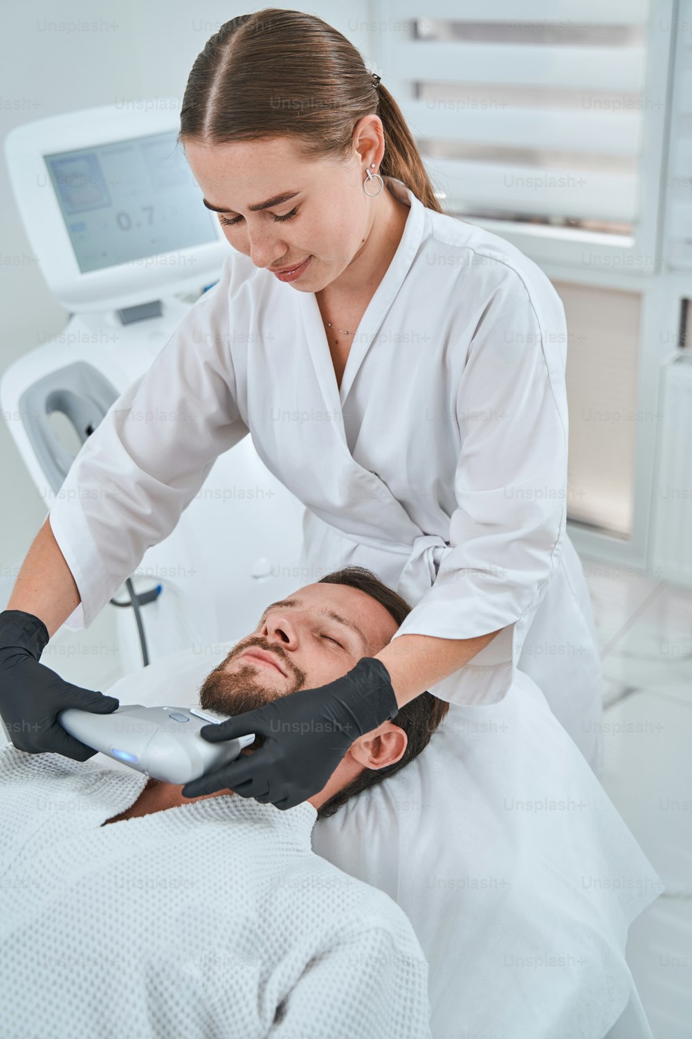 Experienced beautician in nitrile gloves carrying out the high-intensity focused ultrasound treatment on the patient chin