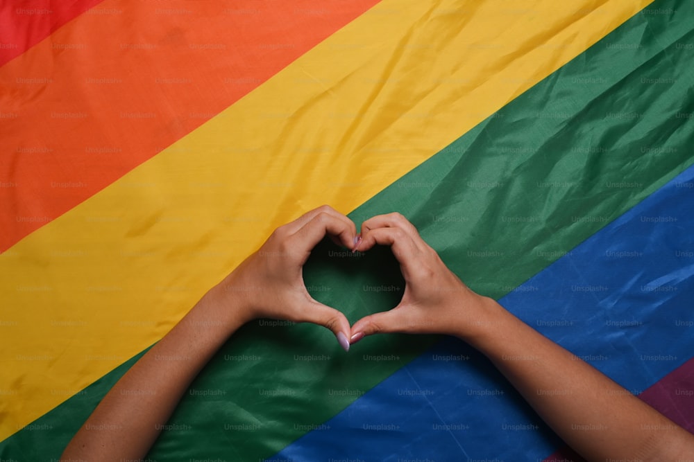 LGBT 레즈비언 커플 손은 무지개 LGBT 깃발 위에 하트 모양을 취했습니다. LGBT 자부심의 개념.