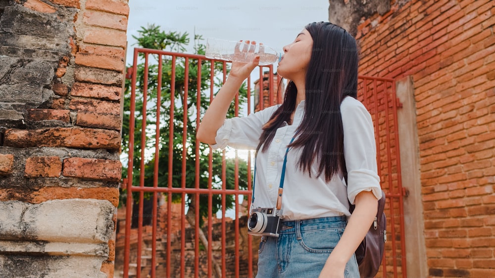 Junge asiatische Backpackerin Bloggerin Tourist mit Kamera fühlen sich müde stehen vor der Pagode, machen eine Pause und trinken Wasser in Plastikflasche in der Altstadt, Lifestyle touristisches Reiseurlaubskonzept.