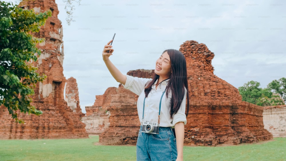 Young Asian backpacker blogger woman casual take selfie video call on mobile phone sharing live online for audience travel together at pagoda old city, Lifestyle tourist travel holiday concept.