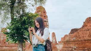 陽気で美しい若いアジアのバックパッカーブロガーの女性は、スマートフォンの写真を見てカジュアルで、古い街で幸せな顔の旅行塔で笑顔、ライフスタイルの観光旅行の休日のコンセプト。
